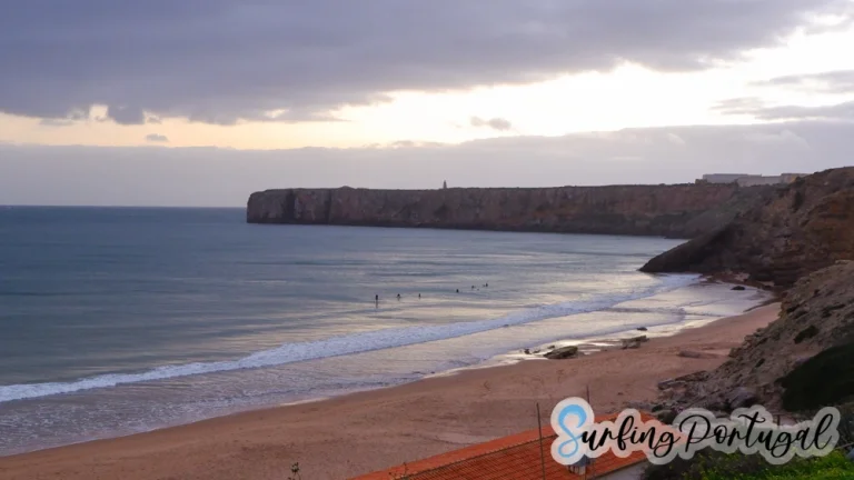 Praia da Mareta looking west to the cape of Sagres with some surfers in the water waiting for waves during the sunset