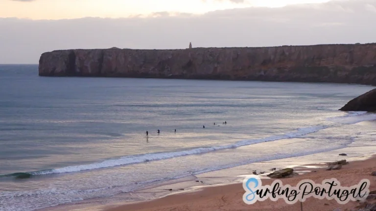 Praia da Mareta looking west to the cape of Sagres with some surfers in the water waiting for waves during the sunset